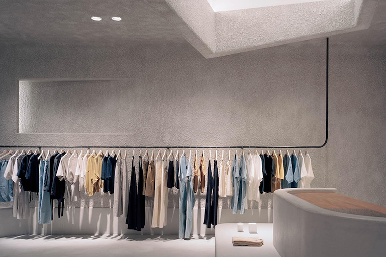 The interior of the Oasis Clothing lobby is made up of smooth canyon walls and has a skylight shining onto a rack of colorful clothing.