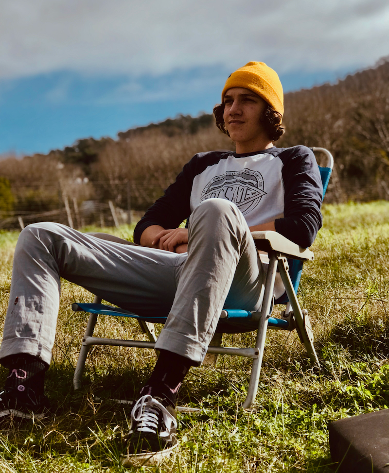 A man wearing gray Oasis men's chino pants sits on the slope of a hill and looks into the distance.