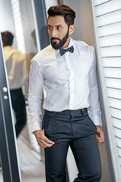 A man leans against the wall in the Oasis white dress shirt with Oasis polka-dotted bowtie