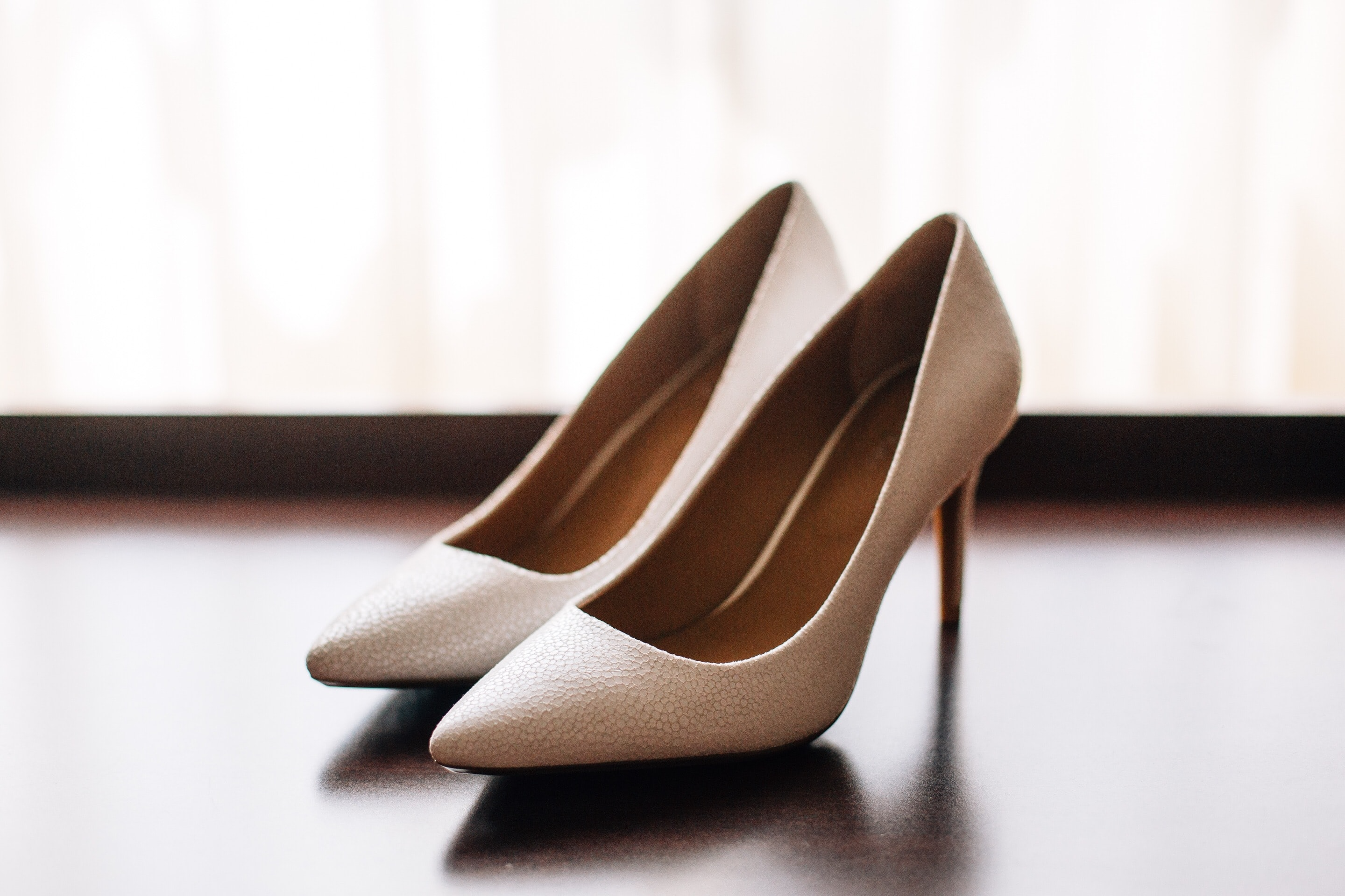 A pair of light brown Oasis heels rest on a wooden floor, illuminated by sunlight.