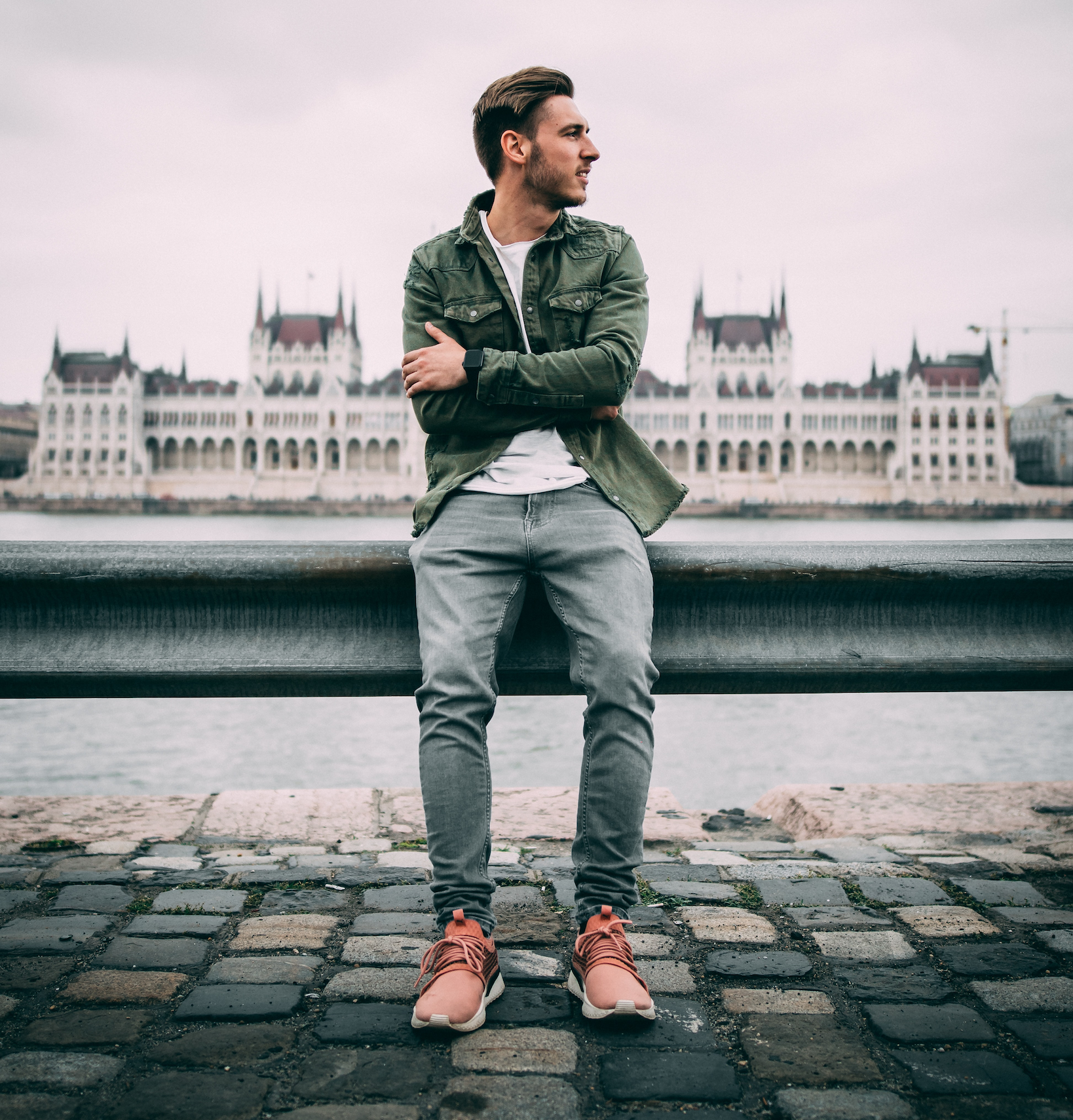 A man leans against the railing in gray Oasis men's slim denim jeans.