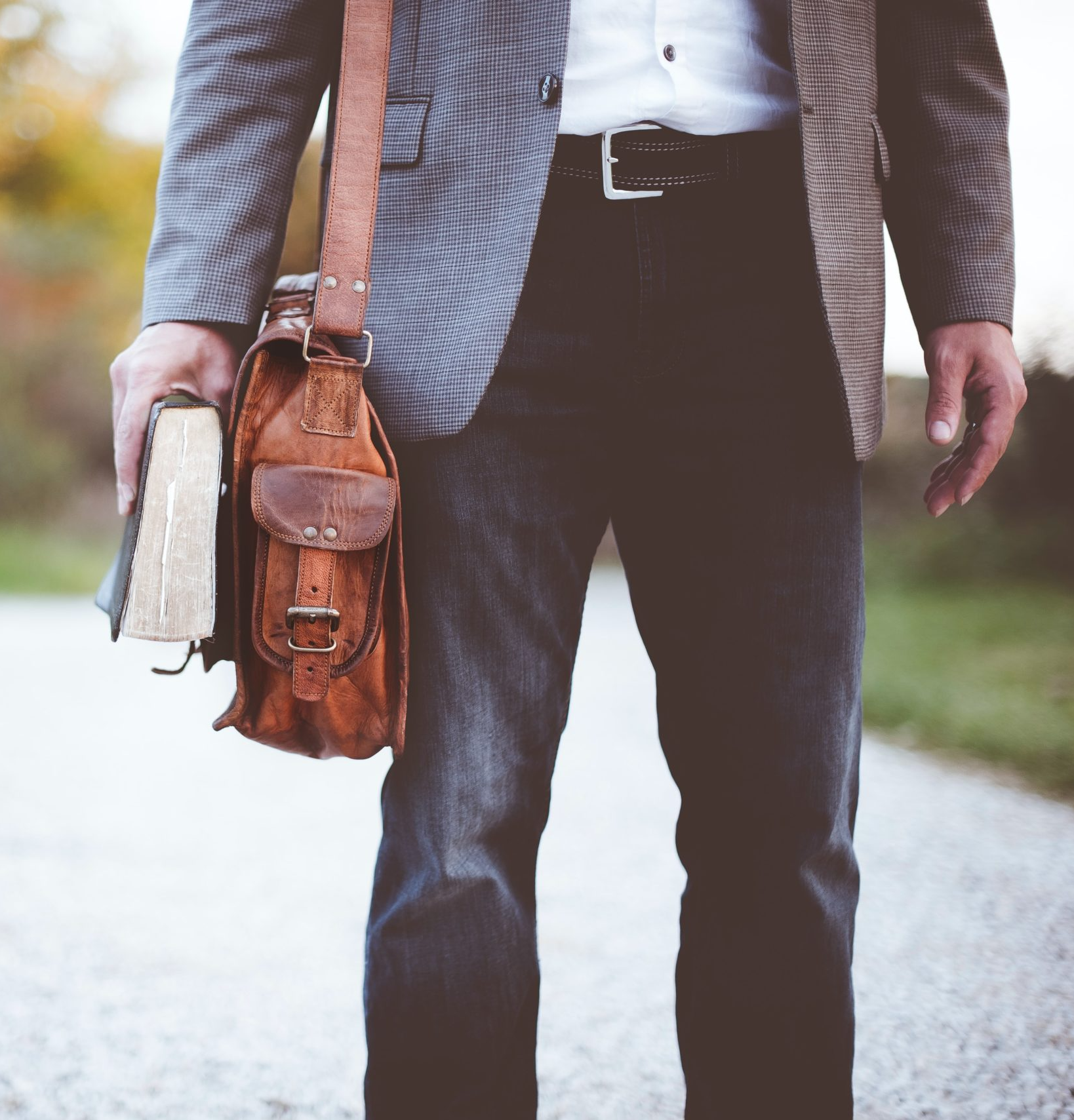 A man wearing a briefcase and holding a book stands in traditional blue denim Oasis jeans.