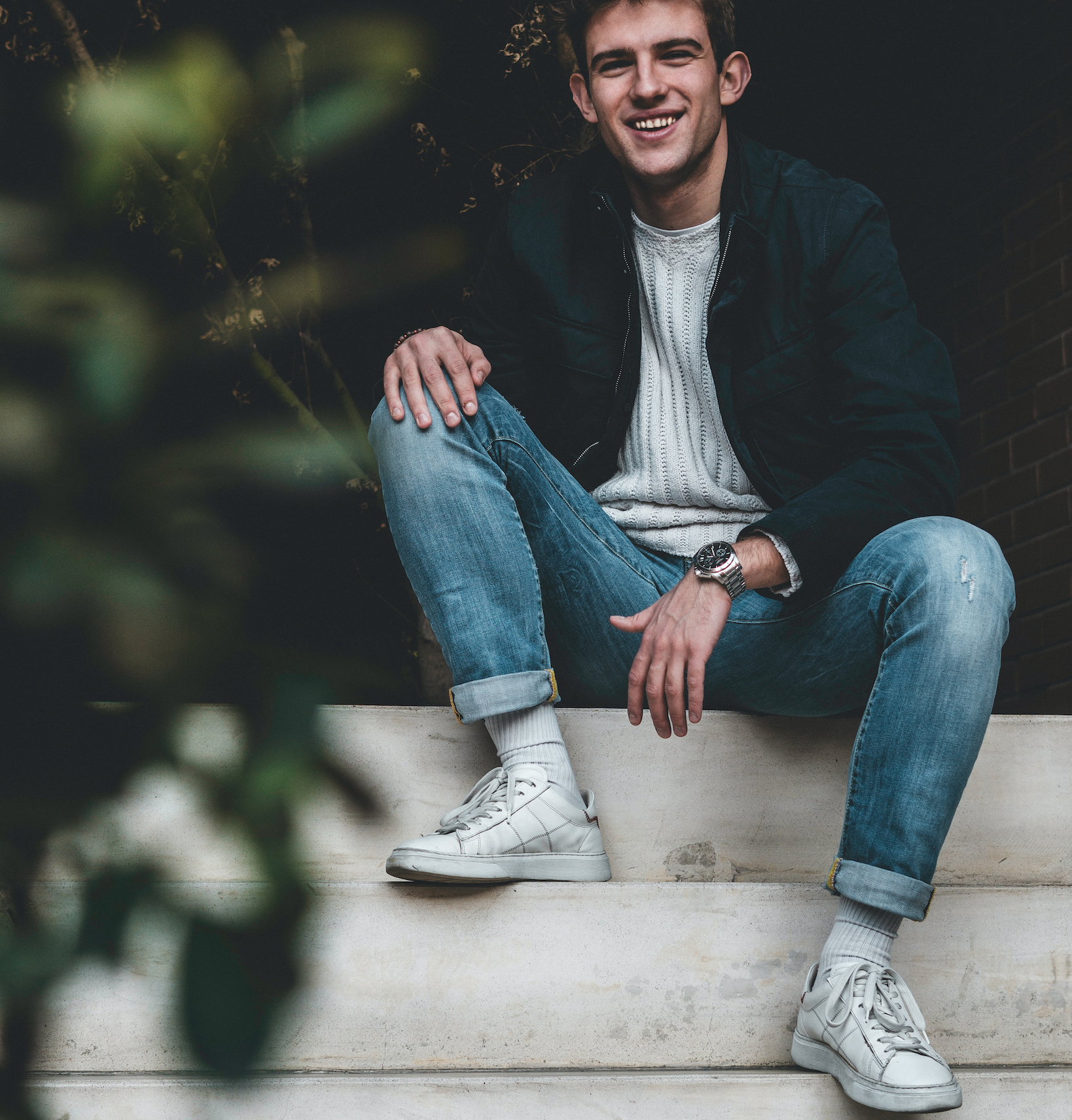 A man smiles into the distance while wearing cuffed and faded light blue Oasis jeans.