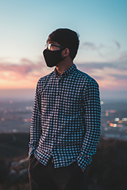 In an age of coronavirus, a masked man looks at the sunset while wearing a blue-white Oasis men's plaid shirt.