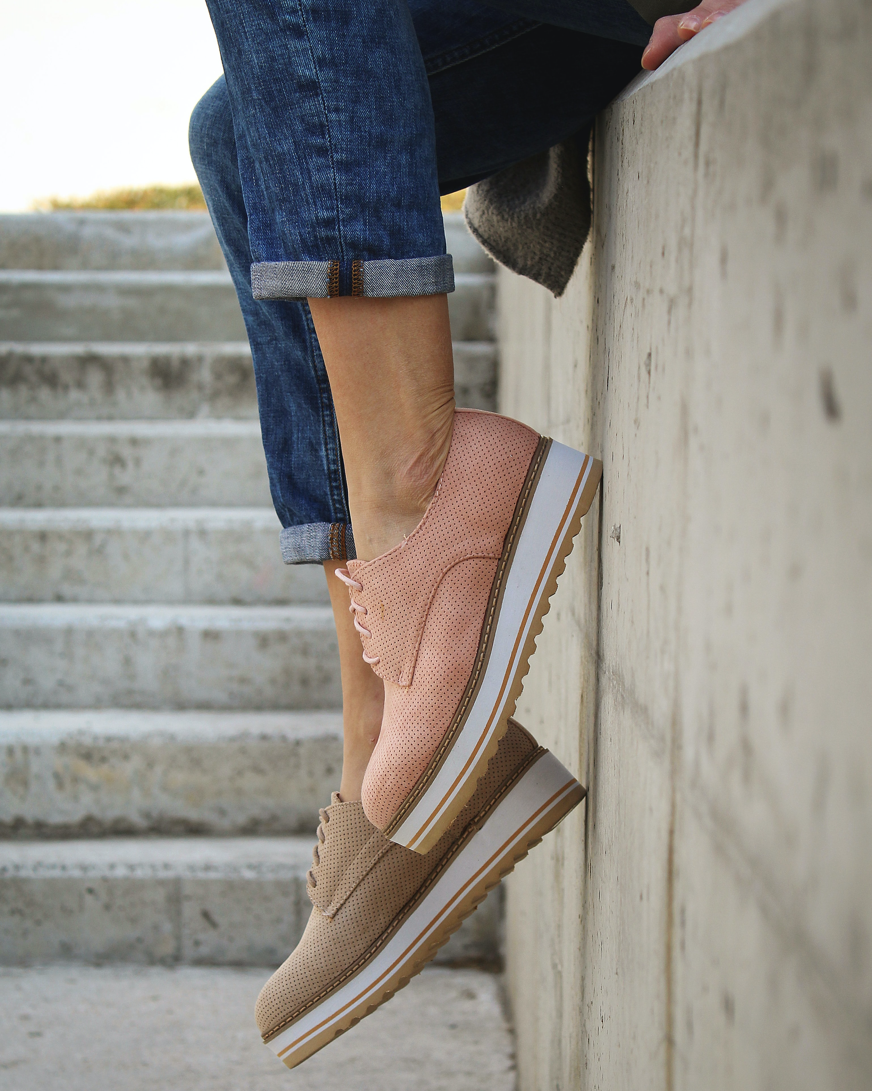 A woman sits on the edge of a wall wearing a pair of rose-colored Oasis sneakers.