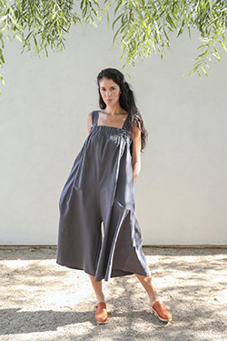 A woman stands in the shade while wearing the breezy Oasis sundress in grayish-blue.