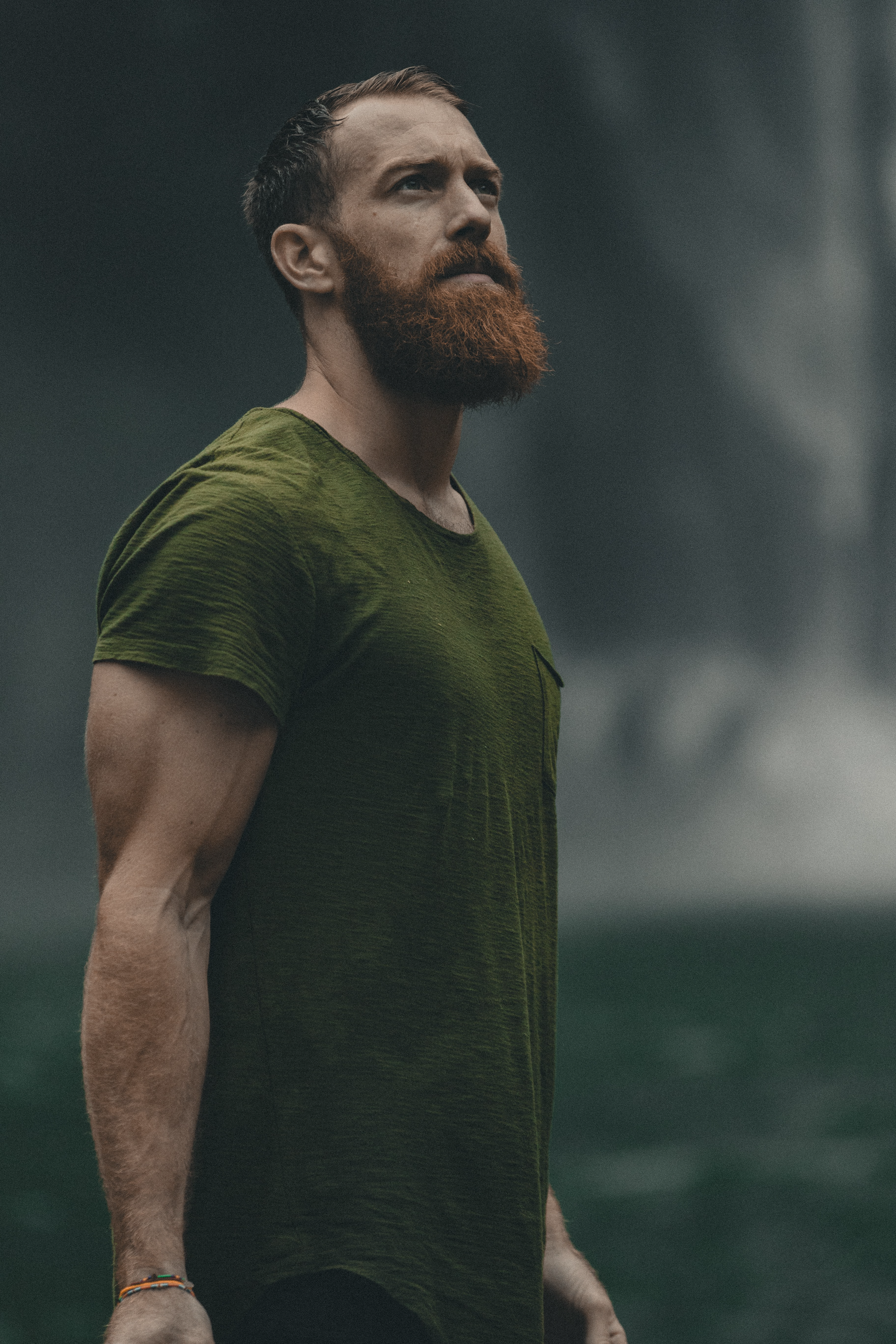 A man looks into the distance while wearing a dark green Oasis men's T-shirt.