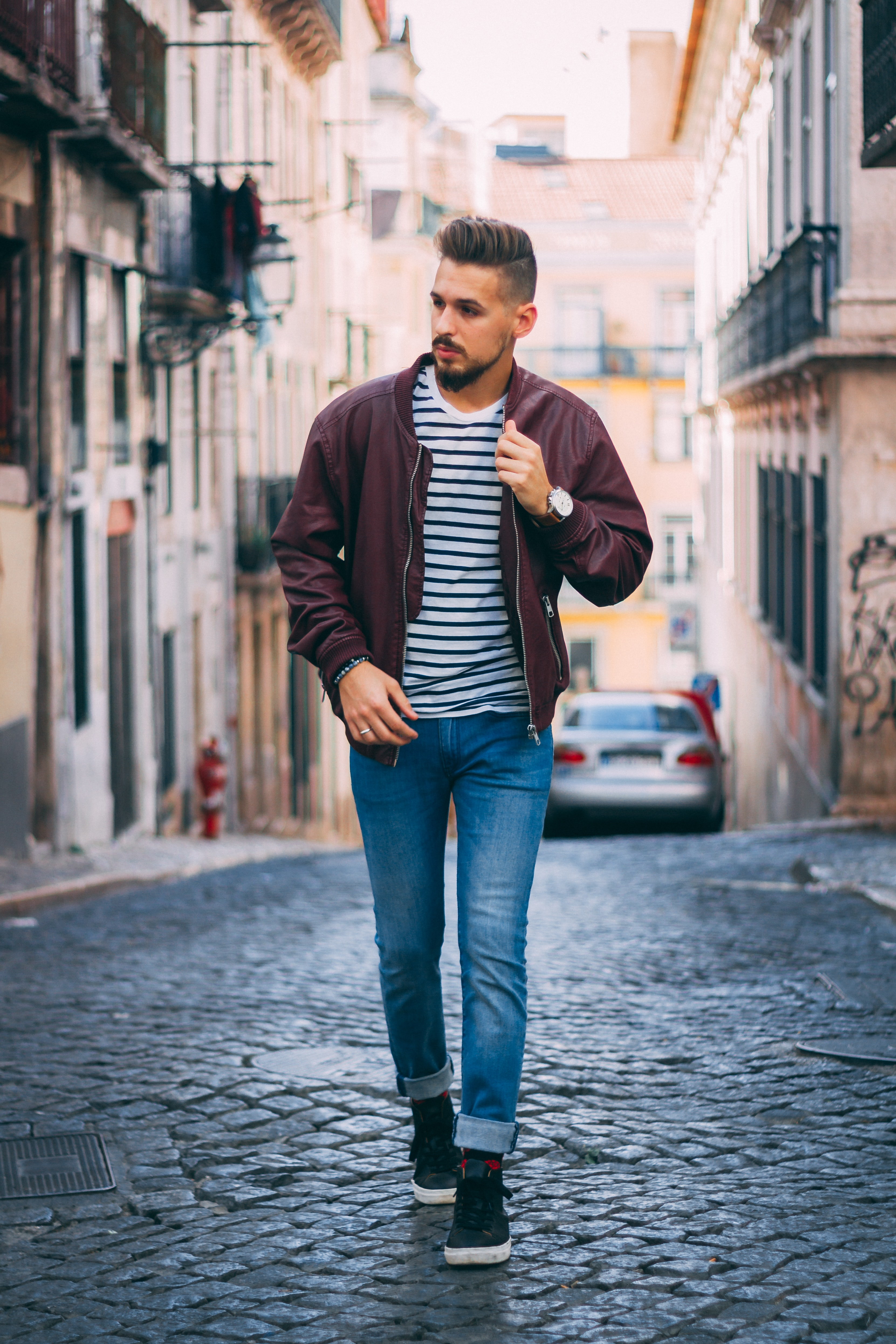 A man wearing a blue striped Oasis men's T-shirt walks through a small town.